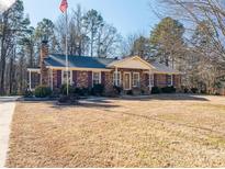 Brick ranch house with mature trees, a large yard, and a flag at 133 Devine St, Stanley, NC 28164