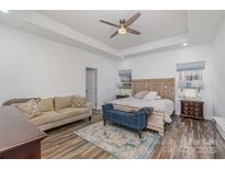 Bright main bedroom featuring a tray ceiling, ceiling fan, sitting area, and decorative rug at 1076 Furnace Rd, Iron Station, NC 28080
