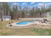 A kidney-shaped pool with a small waterfall feature is surrounded by a stone-paver deck and mature trees at 1076 Furnace Rd, Iron Station, NC 28080
