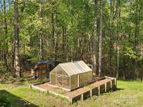 A greenhouse and chicken coop in the backyard surrounded by lush trees and greenery at 888 Brevard Place Rd, Iron Station, NC 28080