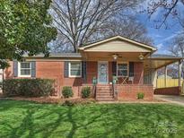 Charming brick home featuring a well-manicured lawn and inviting covered front porch with table set at 833 Montford Dr, Charlotte, NC 28209