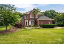 Charming two-story red brick home with well-manicured lawn, mature trees and landscaping, under a sunny sky at 133 Castaway Trl, Mooresville, NC 28117