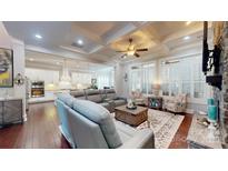 Open-concept living room with hardwood floors, coffered ceilings, and stone fireplace, connected to a modern white kitchen at 407 Blue Bay Ct, York, SC 29745