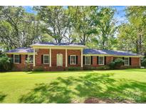 Charming red brick home with a manicured lawn and a classic covered front porch, nestled among mature trees at 1801 Windsor Dr, Lancaster, SC 29720