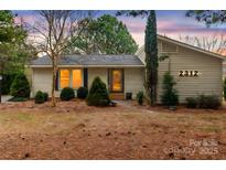 House exterior at dusk, showcasing a light beige color, a neatly trimmed lawn, and mature trees surrounding the property at 2312 Roland Dr, Monroe, NC 28110