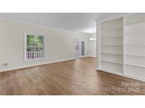 Bright living room with wood floors, large window, built-in shelving, and double glass doors at 5929 Quail Hollow Rd # B, Charlotte, NC 28210