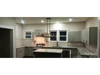 Well-lit kitchen featuring white subway tile backsplash, granite countertops, and gray cabinets at 105 N Inman Ave, Bessemer City, NC 28016