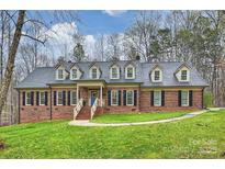Charming brick home with a blue door, dormer windows, black shutters, and a beautifully landscaped lawn at 2305 Beechwood Dr, Waxhaw, NC 28173