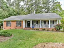 Brick ranch home with front porch and rocking chairs, nestled in a wooded area at 7115 Powder Mill Pl, Charlotte, NC 28277