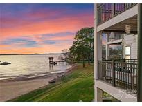 Exterior view of condos with balconies, a tranquil lake view, and a private dock under a colorful sunset sky at 17811 Half Moon Ln # E, Cornelius, NC 28031