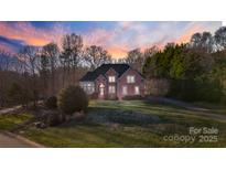 Charming two-story brick home featuring a well-manicured lawn and lush landscaping at sunset at 1020 James Madison Dr, Weddington, NC 28104