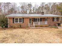 Brick ranch home with metal roof, white porch, and landscaping at 833 E Chestnut St, Stanley, NC 28164
