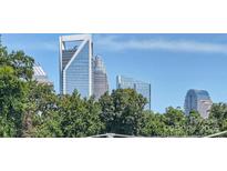 A vibrant city skyline view with modern skyscrapers rising above lush green treetops against a clear blue sky at 619 W Tremont Ave, Charlotte, NC 28203