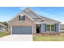Charming home featuring stone accents, a two-car garage, and a well-manicured lawn, creating an inviting curb appeal at 108 Sari St, Troutman, NC 28166