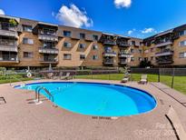 Exterior view of a community pool with lounge chairs at a brick apartment building on a bright, sunny day at 1323 Queens Rd # 308, Charlotte, NC 28207