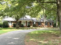 Charming brick home with lush trees, a curved driveway, and a welcoming front porch at 4210 Wrangler Sw Dr, Concord, NC 28027