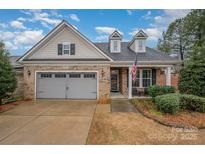 Charming brick home featuring a two-car garage, dormer windows and a cozy front porch with an American flag at 2312 Whispering Way, Indian Trail, NC 28079
