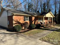 Charming brick home with manicured landscaping, mature trees, and sidewalk leading to the inviting front porch at 8628 Williamsburg Cir, Huntersville, NC 28078