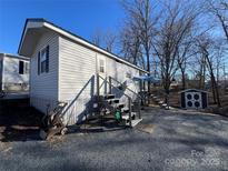 A single-story house with gray siding, gravel driveway, and a storage shed. There are bare trees around the house at 109 Hummingbird Cir, New London, NC 28127