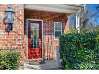 Inviting red front door with glass panels, flanked by lush greenery and a brick facade at 615 Bourton House Dr, Charlotte, NC 28211