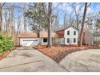 Charming two-story home with white siding, a two-car garage, and a cozy front yard surrounded by mature trees at 9307 Raintree Ln, Charlotte, NC 28277