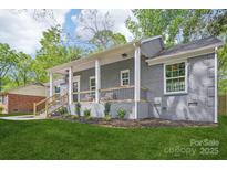 Charming gray brick home featuring a welcoming front porch with wooden railings, lush green lawn and manicured landscaping at 6813 Elm Forest Dr, Charlotte, NC 28212