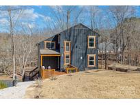 Stunning modern home with a dark exterior, wooden trim, and a spacious deck overlooking the serene lakeside at 27068 Catamaran Dr, Tega Cay, SC 29708