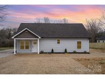 Charming single-story home with gray siding, a brown roof, and a cozy front porch under a beautiful sunset sky at 1010 Wilmouth St, Shelby, NC 28152