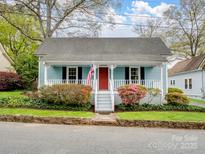 Charming light blue home featuring a welcoming front porch, vibrant landscaping, and a red front door at 253 Misenheimer Nw Dr, Concord, NC 28025