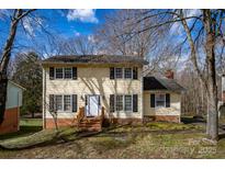 Charming two-story home with a light yellow exterior and black shutters, set against a backdrop of trees and a blue sky at 7708 Ritter Dr, Charlotte, NC 28270
