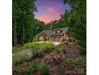 Beautiful stone and brick home with a three-car garage and lush landscaping under a vibrant evening sky at 11280 Mcfalls Dr, Indian Land, SC 29707