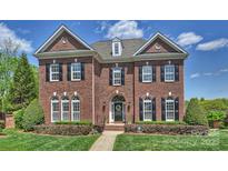 Elegant brick home featuring a manicured lawn, symmetrical design, and black shutters under a partly cloudy sky at 100 Cliveden Ct, Belmont, NC 28012
