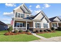 Charming two-story home featuring a covered front porch and manicured lawn under a bright blue sky at 136 Kingston Dr, Locust, NC 28097