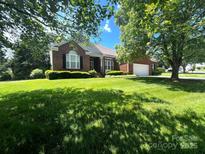 Charming brick home featuring lush green lawn and mature trees creating a serene curb appeal at 7700 Sedgebrook E Dr, Stanley, NC 28164