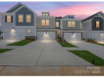 Modern townhomes featuring diverse colors, stone accents, white garages, and well-maintained lawns under a beautiful pink sky at 113 Alluvium Ln, Waxhaw, NC 28173