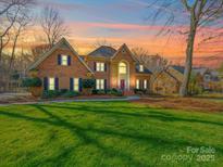 Stunning brick home featuring a well-manicured lawn and mature trees under a beautiful sunset sky at 2217 Blue Bell Ln, Charlotte, NC 28270