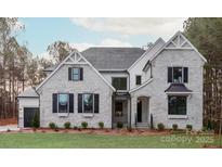 Stunning two-story home showcasing a stone facade, black shutters, and meticulously landscaped front yard at 8328 Victoria Lake Dr, Waxhaw, NC 28173