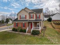 Inviting two-story home boasting a brick facade, red shutters, and a charming front porch at 5032 Meadow Woods Dr, Lowell, NC 28098