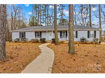 Charming single-story home with light blue siding, black shutters, front porch, and a walkway amidst mature trees at 101 Fairfax Dr, Salisbury, NC 28146