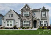 Charming two-story home featuring a stone facade, gray siding, manicured lawn, and professional landscaping at 7133 Sumters Camp Trl, Fort Mill, SC 29707