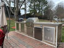 Outdoor kitchen featuring a built-in grill, sink, storage, and mini refrigerator on a brick patio, perfect for entertaining at 8932 Raven Park Dr, Charlotte, NC 28216