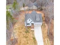 Aerial view of a charming white home with a gray roof, front-facing garage, and long driveway on a wooded lot at 5101 Thornhill Dr, Gastonia, NC 28052
