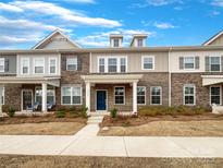 Charming townhome featuring a brick facade, covered entry, and manicured landscaping under a bright, partly cloudy sky at 5220 Kinsbridge Dr, Charlotte, NC 28227