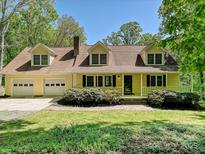 Charming yellow two-story home featuring a welcoming front porch, dormer windows, and attached two car garage at 124 Canterbury Ln, Matthews, NC 28104