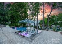 An inviting pool with lounge chairs and clear water is surrounded by beautiful landscaping and mature trees at sunset at 20338 Christofle Dr, Cornelius, NC 28031