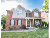 Charming two-story brick home with a manicured lawn, rocking chairs on the front porch, and black shutters at 10836 Clark St, Davidson, NC 28036