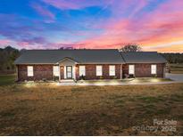 Charming brick home featuring a metal roof and a well-manicured lawn under a colorful twilight sky at 515 Panhandle Rd, Gold Hill, NC 28071