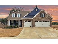 Beautiful brick home showcasing a 2-car garage, dark blue accents, and manicured front yard, set against a scenic sunset at 1300 Dali Blvd, Mount Holly, NC 28120