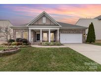Charming brick home with a manicured lawn, covered porch, and two car garage, set against a beautiful sunset sky at 9795 Shearwater Nw Ave, Concord, NC 28027