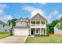 Inviting two-story home featuring a covered porch, attached two-car garage, and manicured lawn on a sunny day at 5116 Heathland Dr # 76, Charlotte, NC 28215